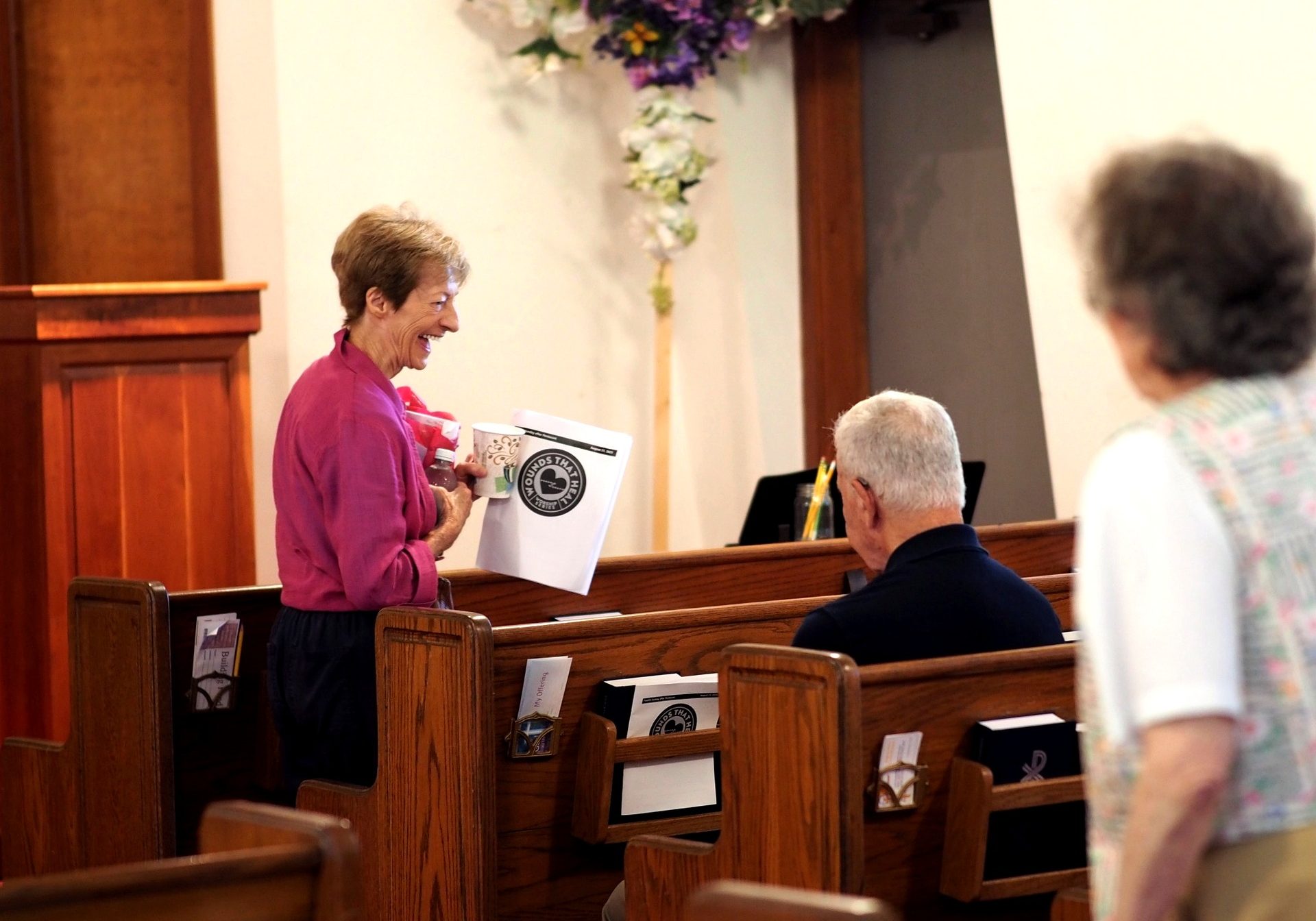 Woman handing a church bulletin to a seated congregant inside a church sanctuary